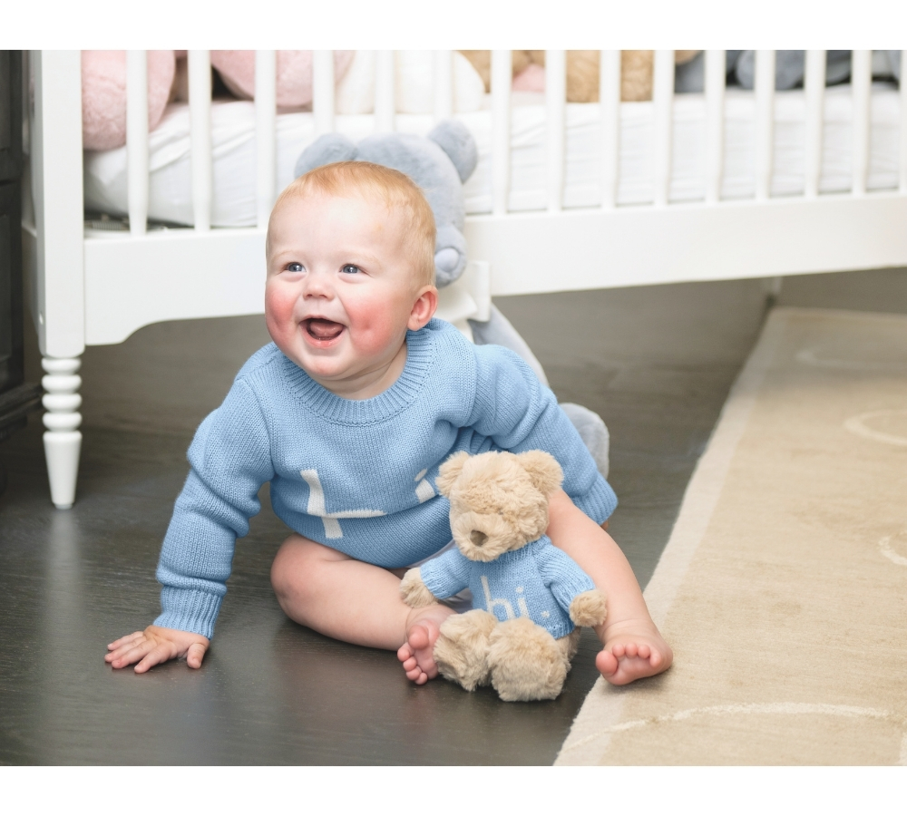 Baby wearing a blue sweater and sitting beside a coordinating plush bear